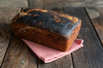 A loaf of homemade bread lies on a kitchen napkin, on a wooden table.