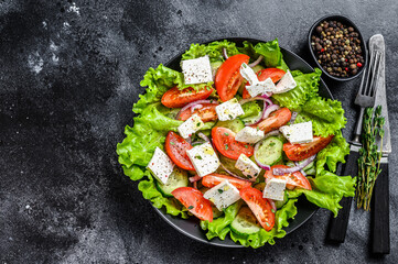 Fresh Greek salad with vegetables and feta cheese in a plate. Black background. Top view. Copy space