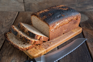 Sliced homemade bread lies on a kitchen board, on a wooden background.