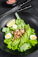 Fresh seafood salad with grilled shrimps prawns, egg, avocado and cucumber in a plate. Black background. top view