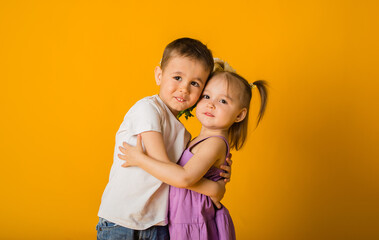 portrait of a little boy and a girl embracing on a yellow background with space for text
