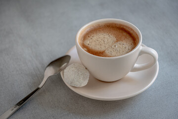 A cup of coffee with candy on a saucer and a metal spoon. On a gray background.