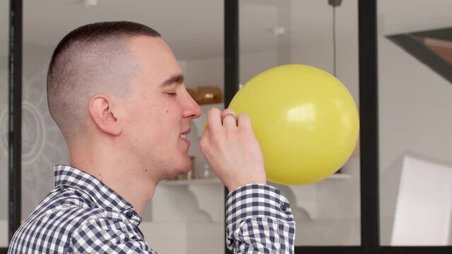 Close-up father man preparing for holiday birthday party, portrait of caucasian millennial guy doing effort inflates balloon inhales air into yellow bubble looking at camera, celebration concept