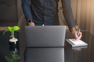 Man working and write on notebook with laptop on desk with sun light morning
