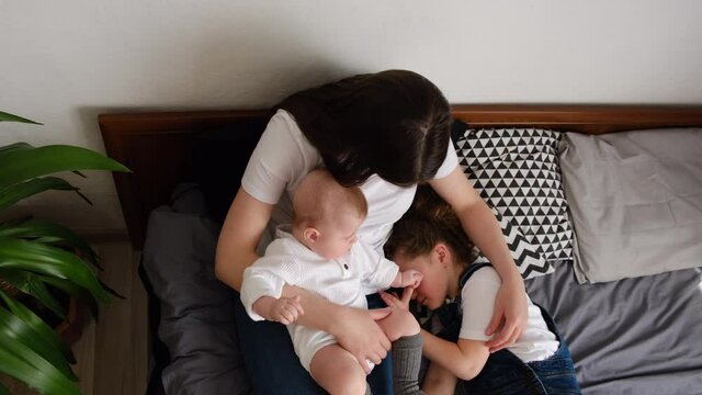 Top view of loving young mom hug cuddle sweet infant toddler with sleeping daughter lying on comfy bed, happy caring caucasian mother embrace lull two small girl sister child, enjoy tender moment