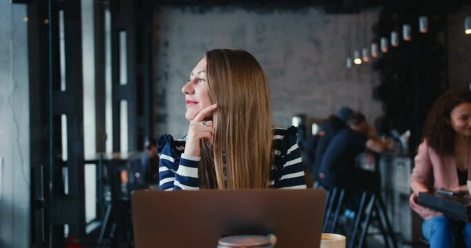 Inspiration concept. Portrait of happy female 30s blonde Caucasian freelance writer using laptop at light modern cafe.