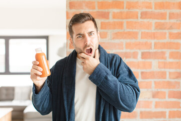 handsome man with mouth and eyes wide open and hand on chin, feeling unpleasantly shocked, saying...