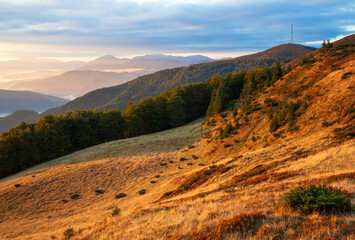 Autumn morning mountain view with sunbeams through haze and low clouds.