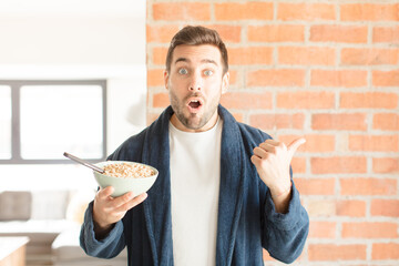 handsome man looking astonished in disbelief, pointing at object on the side and saying wow,...