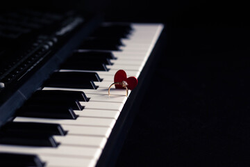 Engagement ring and small heart on a piano with dark background