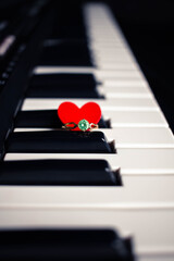 Engagement ring and small heart on a piano with dark background