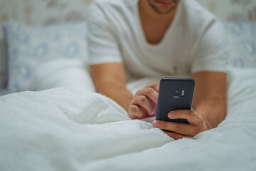 Men lying on the white bed and playing smartphones during night time. Health and social Concept