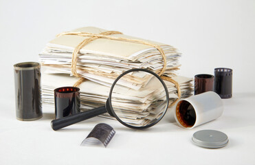 A stack of old photographs, a magnifying glass, negatives on a white background.
