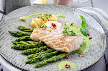 Modern style traditional fried skrei cod fish steak with green asparagus and potatoes served as...