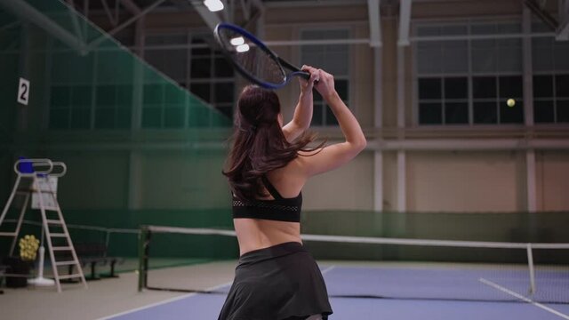 young female tennis player is playing tennis on indoor court, running and hitting ball, slow motion shot, medium shot indoor