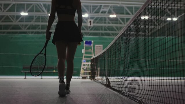 young female tennis player is walking along net on court, back view of slender sporty figure, sport hobby