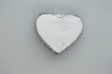 Chocolate candy wrapper in silver color. Heart shape on a gray background. Isolated. Copy the space.