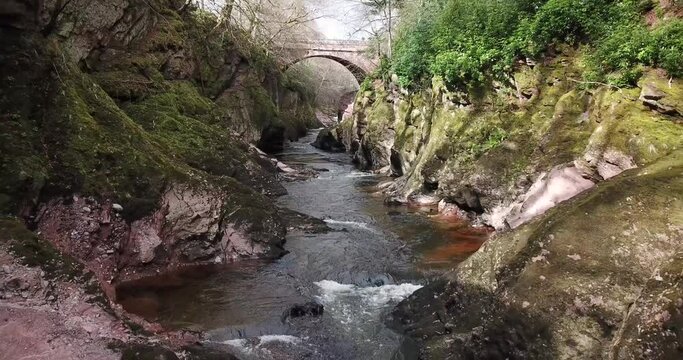 4k aerial footage of gorge and bridge at River North Esk near Edzell, Scotland. Flowing river, rocks and lush vegetation.