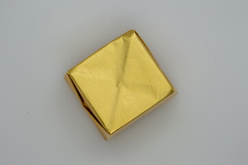 Golden chocolate candy wrapper in the form of a square shape on a gray background. Isolated. Copy...