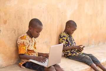 one african kid using a laptop and the other using a mobile phone