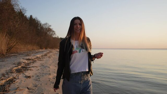 European ethnicity girl walks by the sea. Beautiful woman walks along the shoreline of a lake in a landscape city and comes back and laughs at the camera. Slow motion 4K video of a girl with happy emo