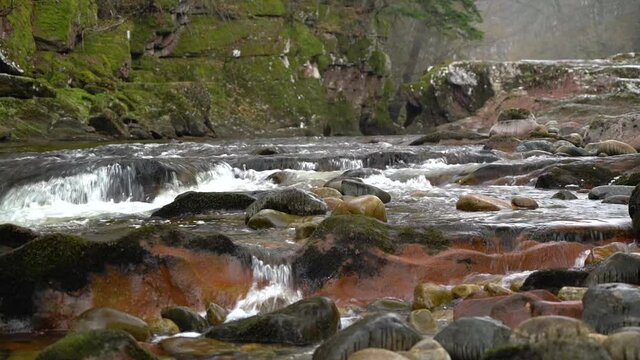 Close up with selective focus of rocks on River North Esk, Angus, Scotland with water flowing over rocks. Light rain is falling.