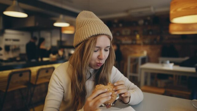 American style. Young woman eating burger in fast food restaurant. People eat unhealthy meal. Getting satisfaction from unhealthy food. Junk food, modern life concet.