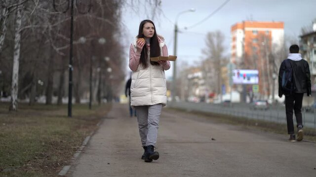 Pretty woman walking outdoors in the city and eating burger