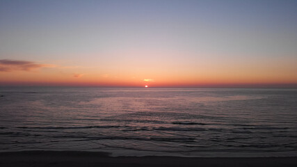 Aerial view of the sea, beach boulders and waves at sunset. Beautiful sunset with flying birds. Waves crashing on sandy beach. Beach with sand dunes and dusk sky in Ofir, Fao, Portugal.