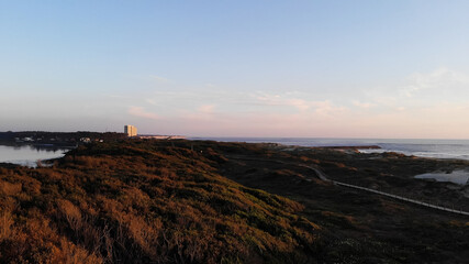Aerial view of the Northern Litoral Natural Park in Ofir, Esposende, Portugal. Wooden boardwalk and the Ofir Towers in the background. Sea, beach boulders, pebble shore and waves at sunset.