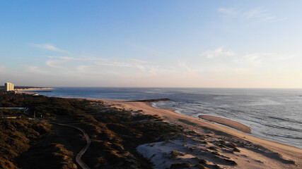 Aerial view of the Northern Litoral Natural Park in Ofir, Esposende, Portugal. Wooden boardwalk and the Ofir Towers in the background. Sea, beach boulders, pebble shore and waves at sunset.