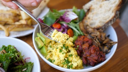 A fork picks up a tofu omelette and shows it to the camera. Plant based Buddha bowl