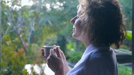 Side view of woman smells her hot morning coffee standing outside enjoying Balinese nature 