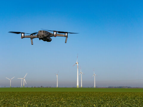 Drone flies over a field. In the background you can see wind turbines and the blue sky. Copy space