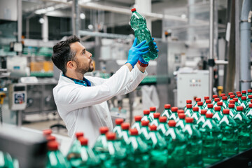 Male worker in bottling factory checking water bottles before shipment. Inspection quality control.