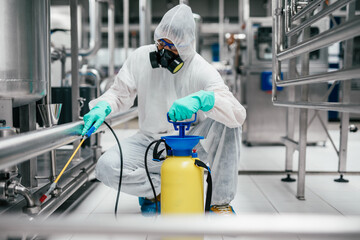 Exterminator in industrial plant spraying pesticide with sprayer. Disinfection of the factory due to the coronavirus epidemic.