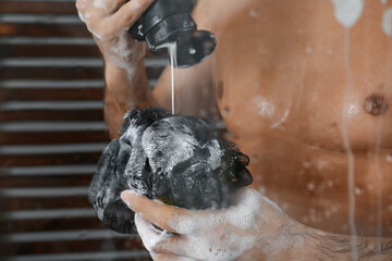 Man applying gel onto mesh pouf in shower at home, closeup