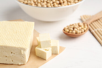 Cut tofu and soya beans on white wooden table, closeup