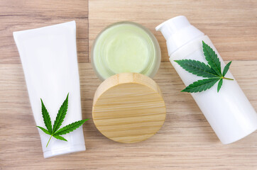 Flat lay of CBD lotion in glass container with Cannabis leaf on wooden backdrop