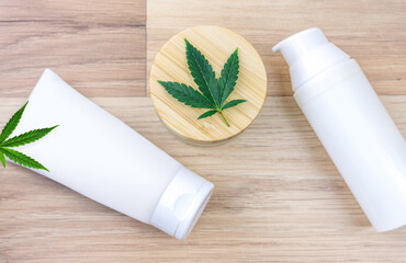 Flat lay of CBD lotion in glass container with Cannabis leaf on wooden backdrop with copy space