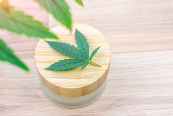 Cannabis CBD lotion in glass container with Cannabis leaf in wooden table