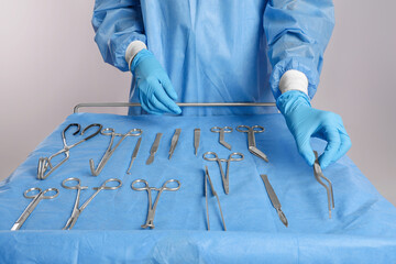 Doctor holding medical forceps near table with different surgical instruments on light background,...