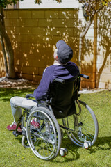 Disabled young man sitting in a wheelchair and taking fresh air in his garden and enjoying life.