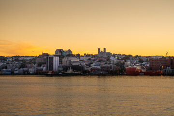 Obraz premium St. John's, Newfoundland, waterfront harbour at night during sunset. The lights on the water are bright yellow and orange which are reflecting from the skyline in the stillness of the smooth water. 
