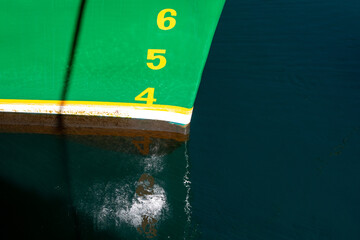 The bow of a large green ship with brown and white stripes at the waterline. The numbers 4, 5, and...