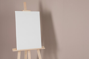 Wooden easel with blank canvas on beige background. Space for text
