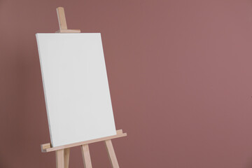 Wooden easel with blank canvas on dusty rose background. Space for text