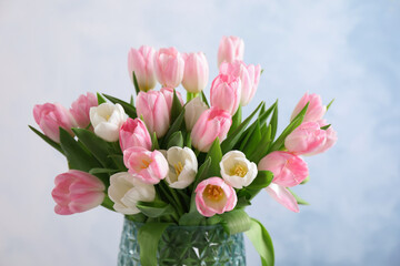 Beautiful bouquet of tulips in glass vase against light background