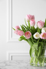 Beautiful bouquet of tulips in glass vase on white marble table