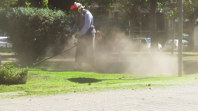Hombre trabajando cortando el pasto en la v&iacute;a publica, con maquina de c&eacute;sped 